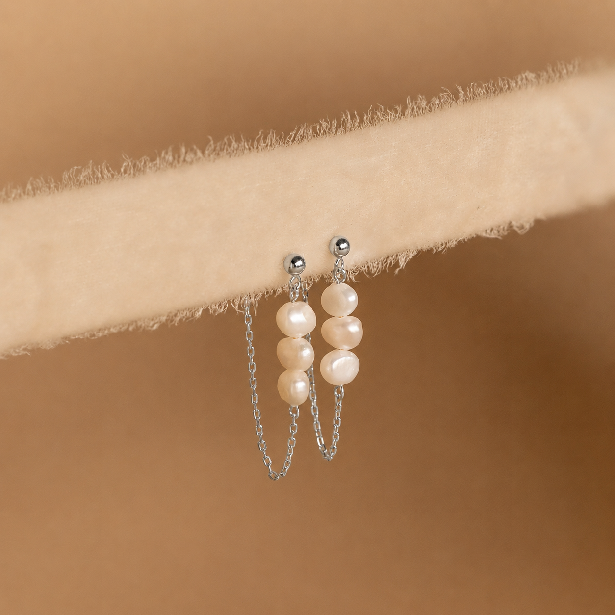 Pearl earrings with silver chains on a beige fabric background