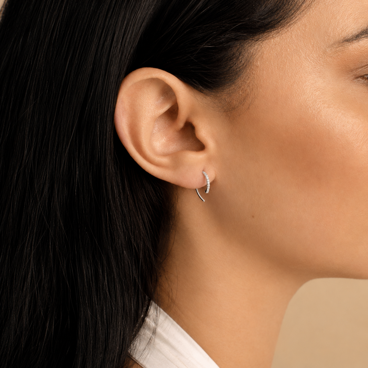Close-up of an ear wearing a diamond hoop earring with dark hair and beige background