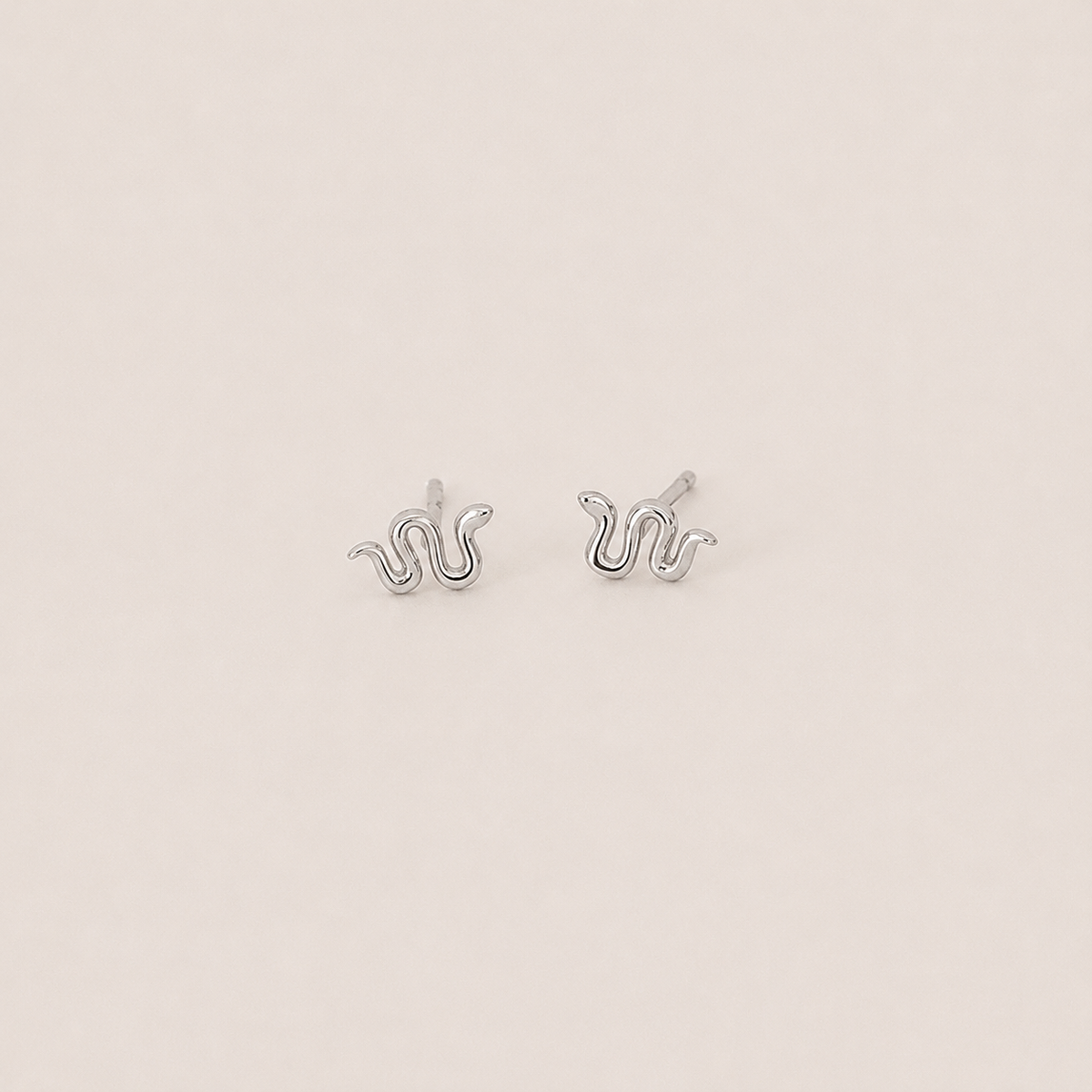 Silver snake-shaped earrings on a light beige background