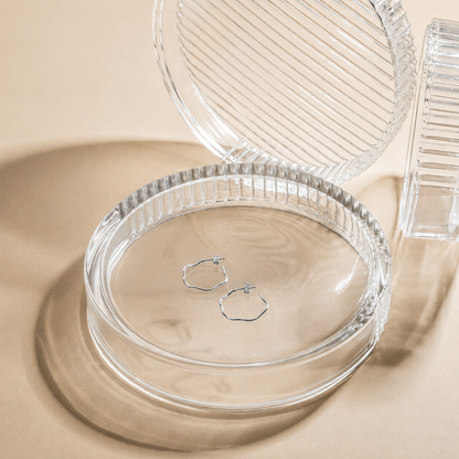 Clear jewelry dish with a pair of silver hoop earrings on a beige background