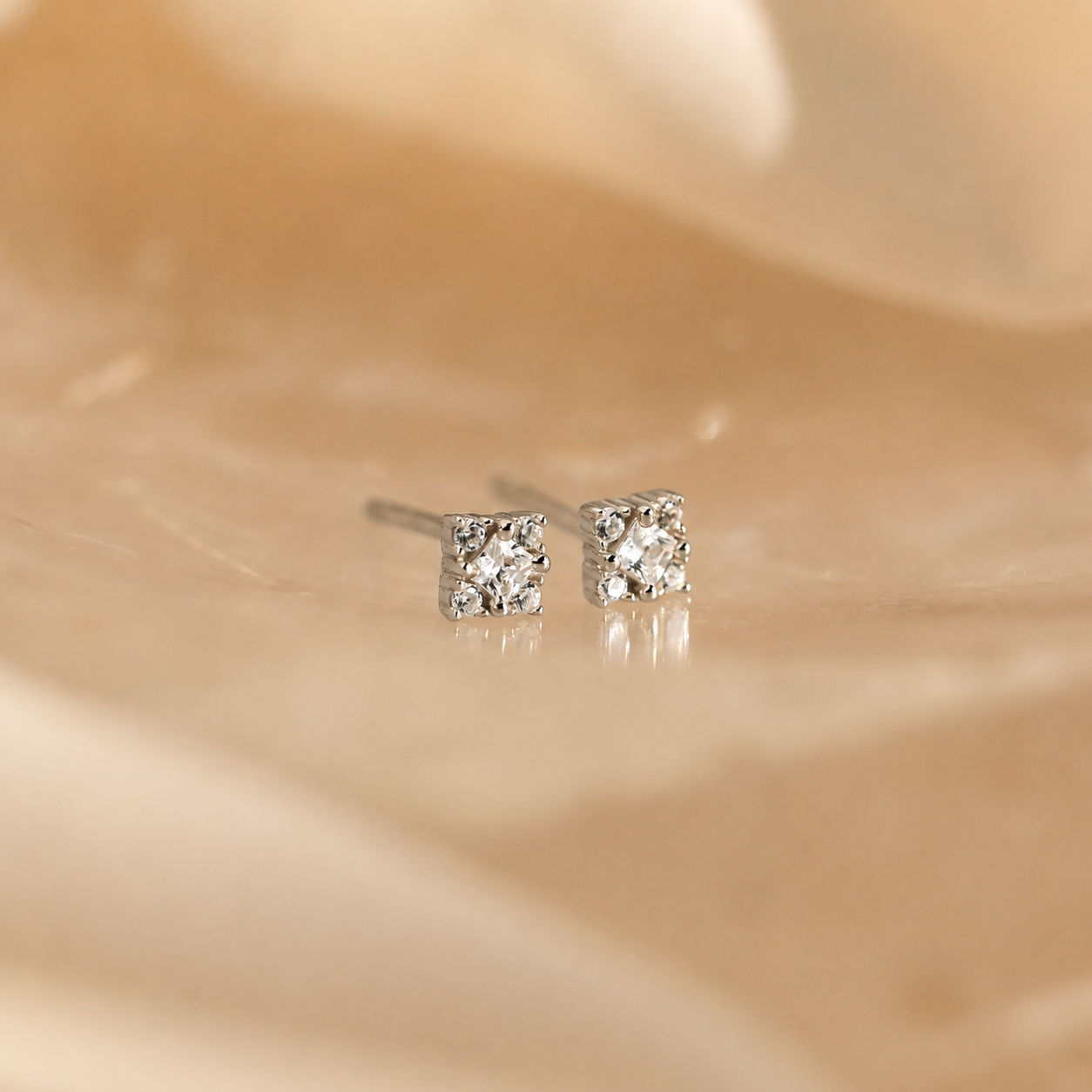 Pair of diamond stud earrings on a beige fabric background