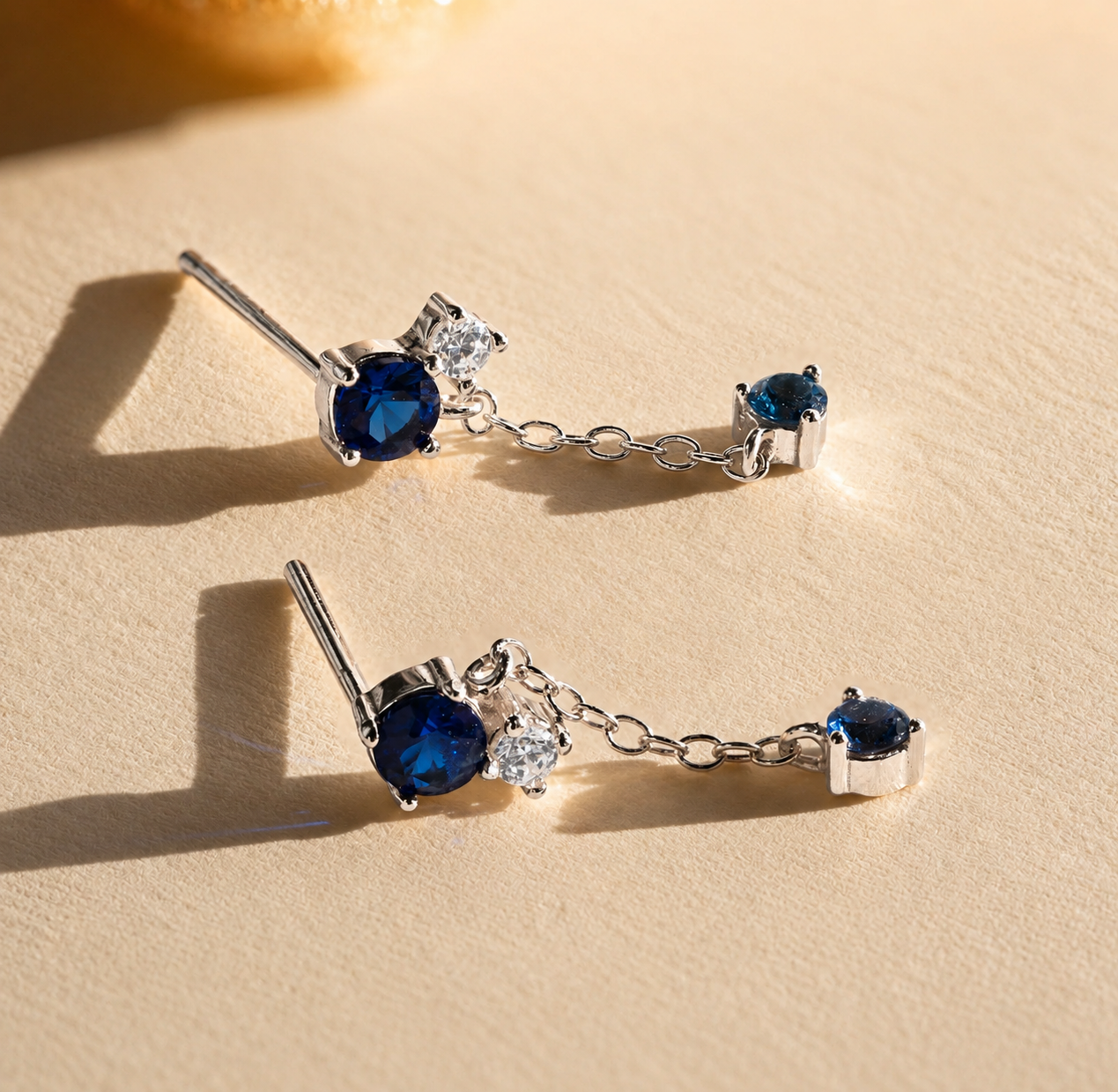 Pair of silver earrings with blue gemstones on a beige surface