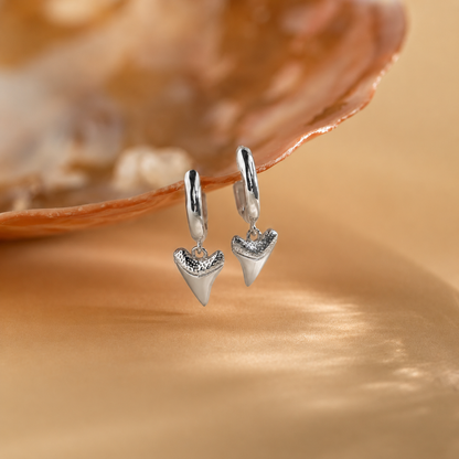 Silver shark tooth earrings on a beige shell background