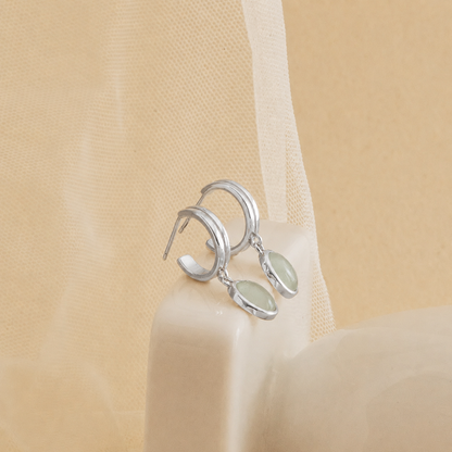Silver earrings with green stones on a beige fabric background