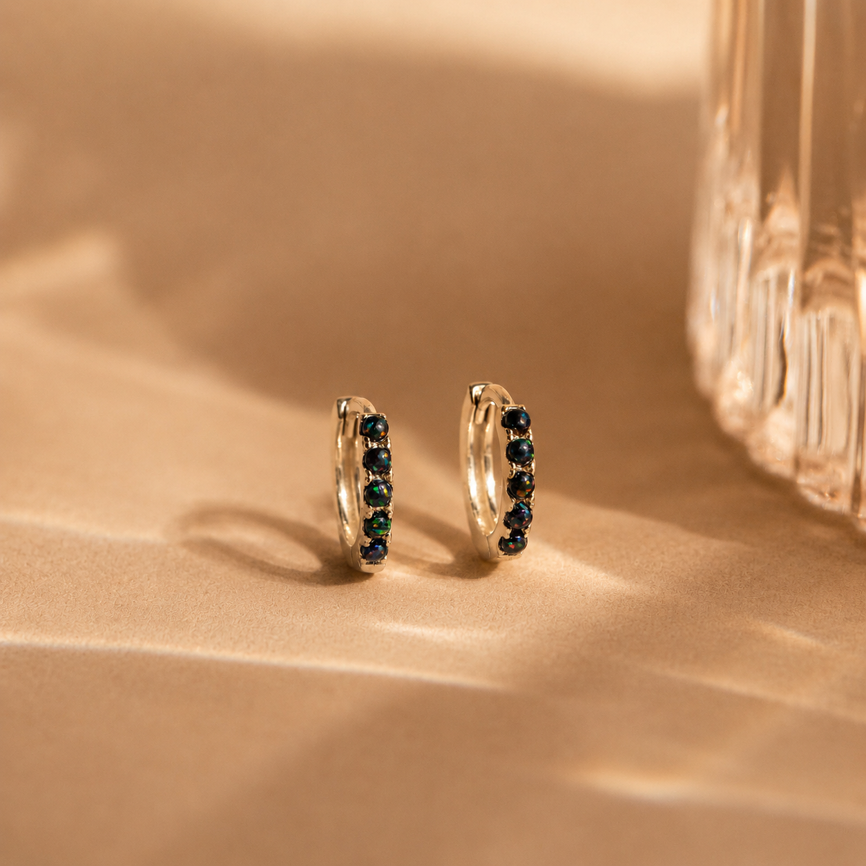 Gold hoop earrings with green gemstones on a beige surface