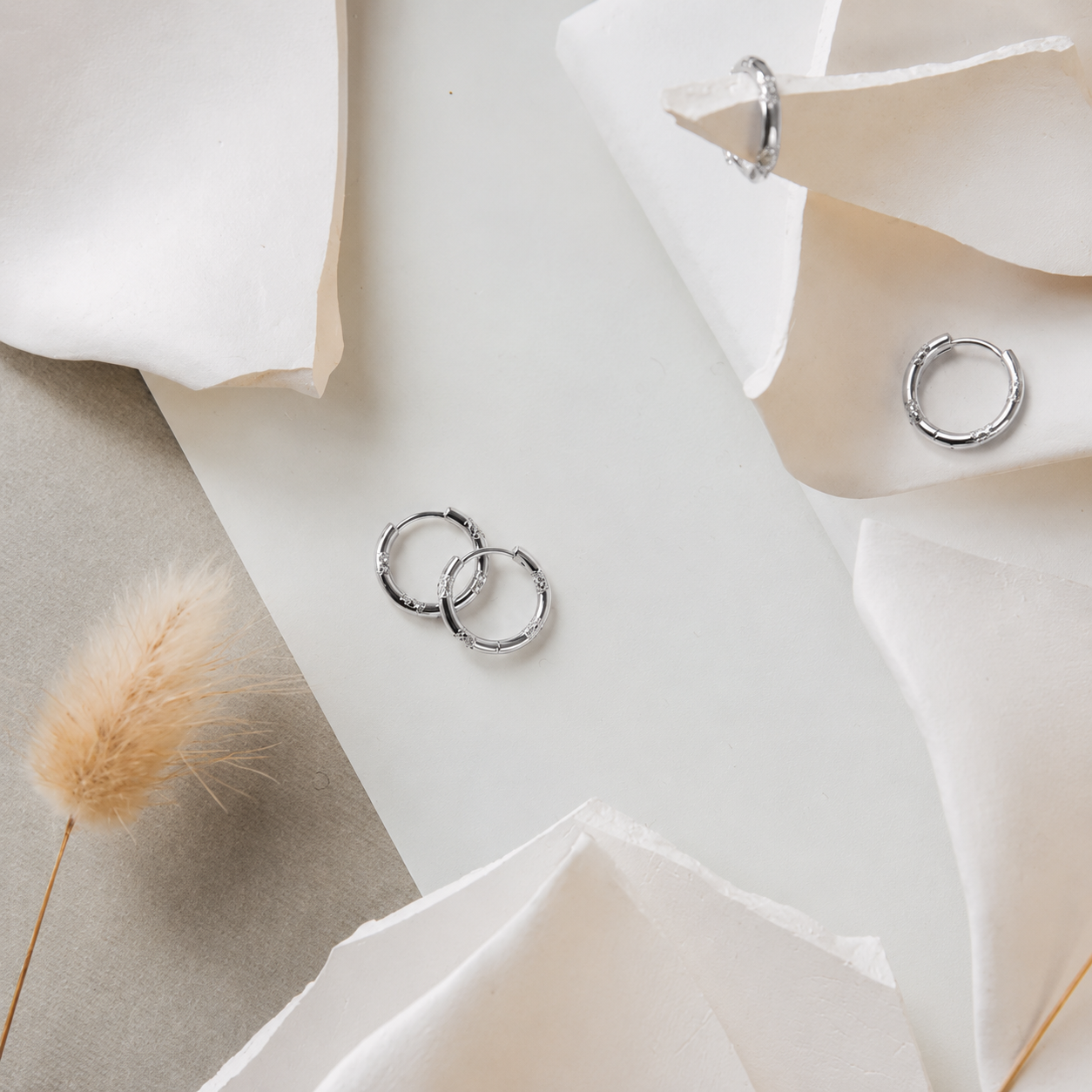 Silver hoop earrings on a white surface with flowers and dried grass.