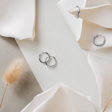 Silver hoop earrings on a white surface with flowers and dried grass.