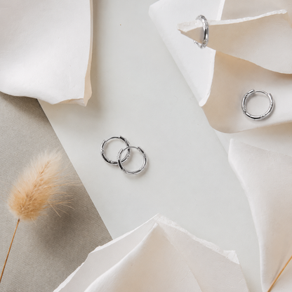 Silver hoop earrings on a white surface with flowers and dried grass.