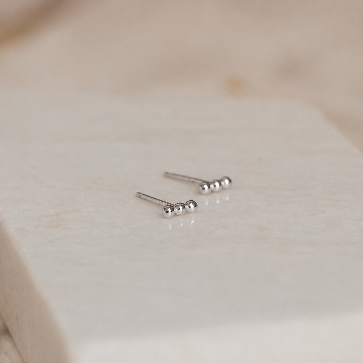 Pair of silver stud earrings on a light beige fabric background