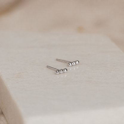 Pair of silver stud earrings on a light beige fabric background