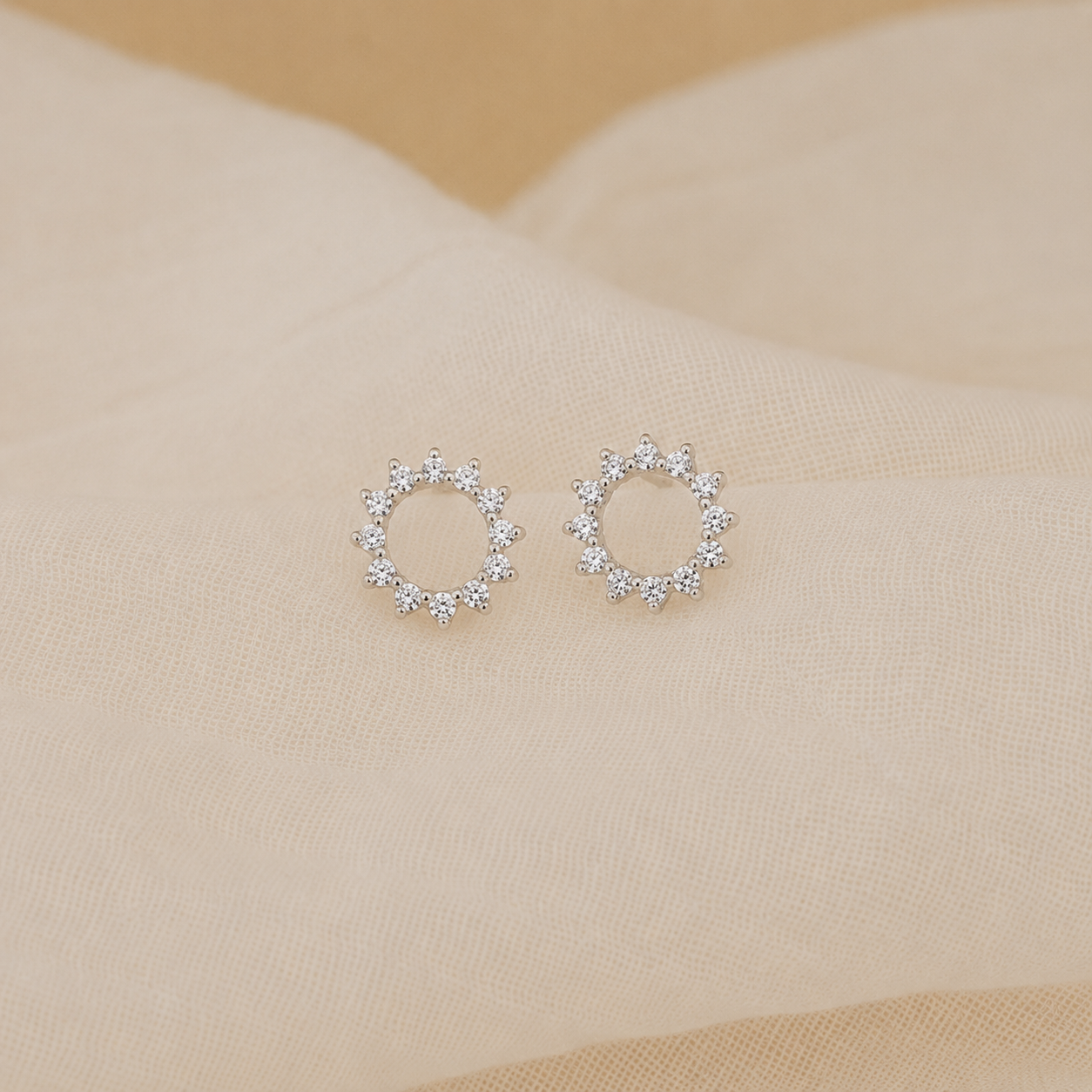 Pair of silver hoop earrings with clear stones on a beige fabric background