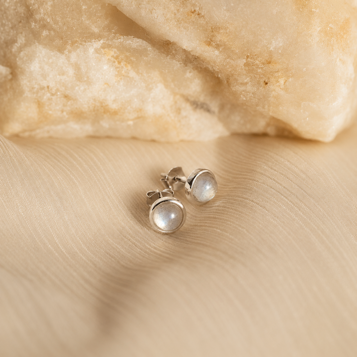 Pair of silver earrings with a gemstone on a beige fabric background