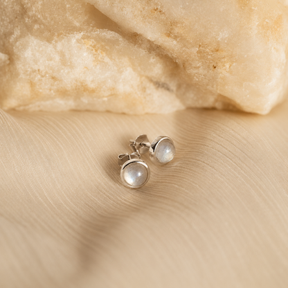 Pair of silver earrings with a gemstone on a beige fabric background