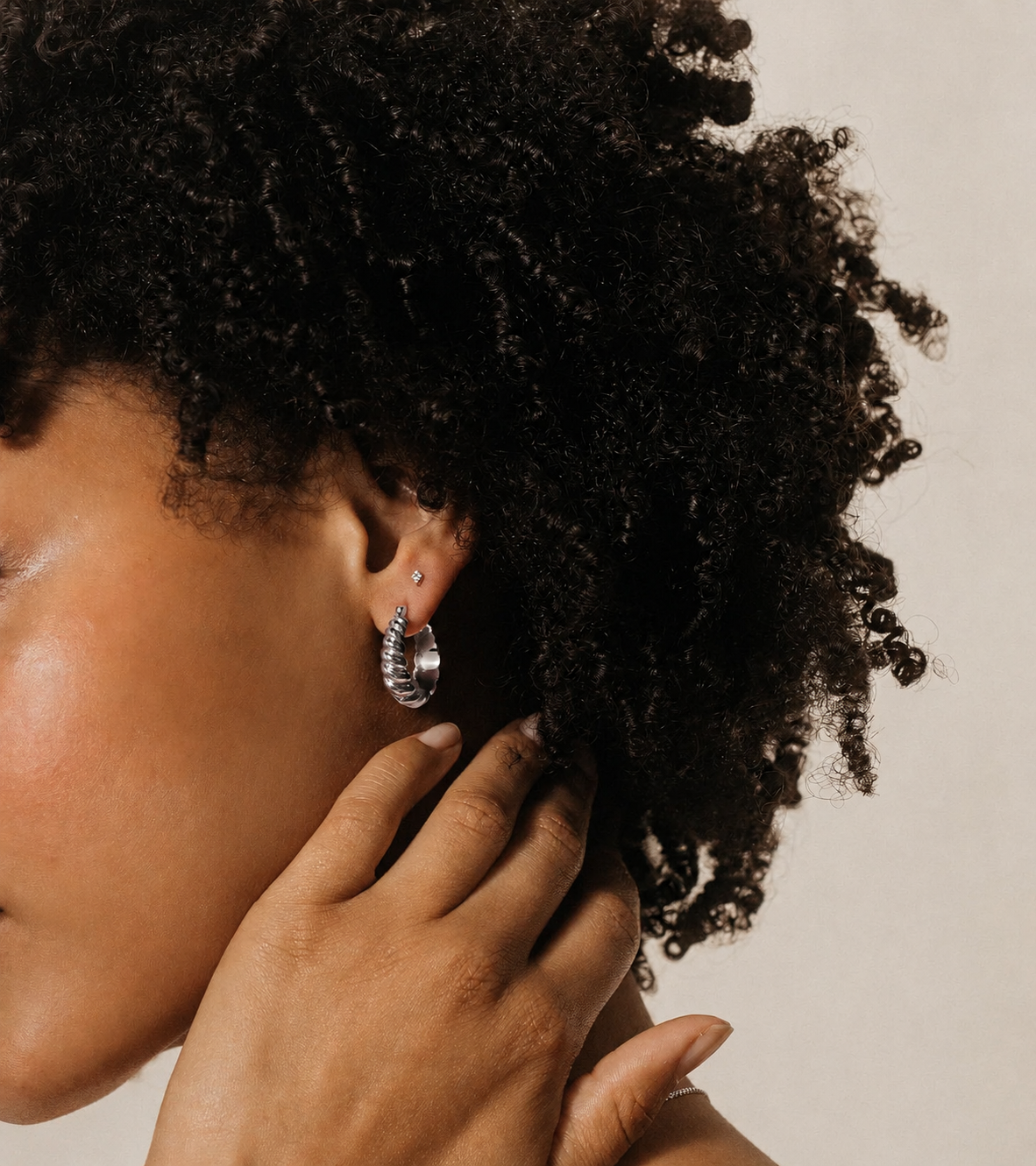 Close-up of a person with textured hair wearing hoop earrings against a neutral background