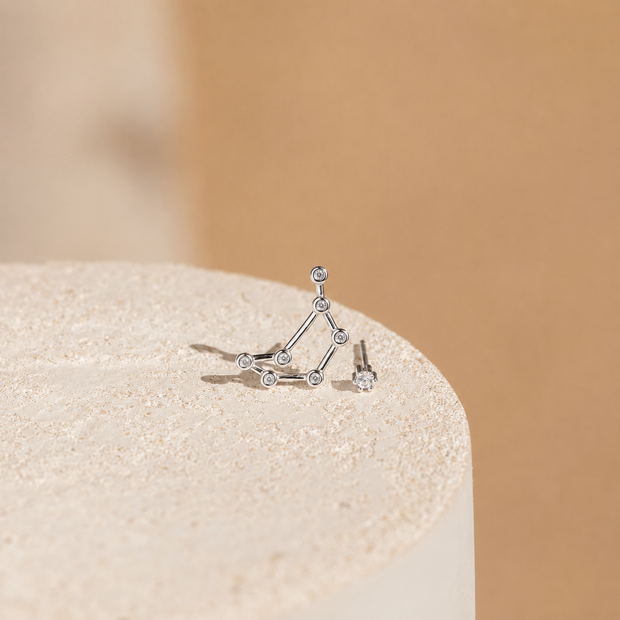 Silver geometric earring on a beige stone with a beige background