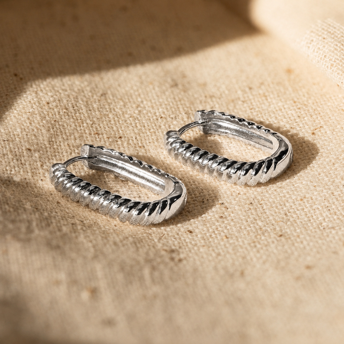 Pair of silver hoop earrings on a textured beige surface