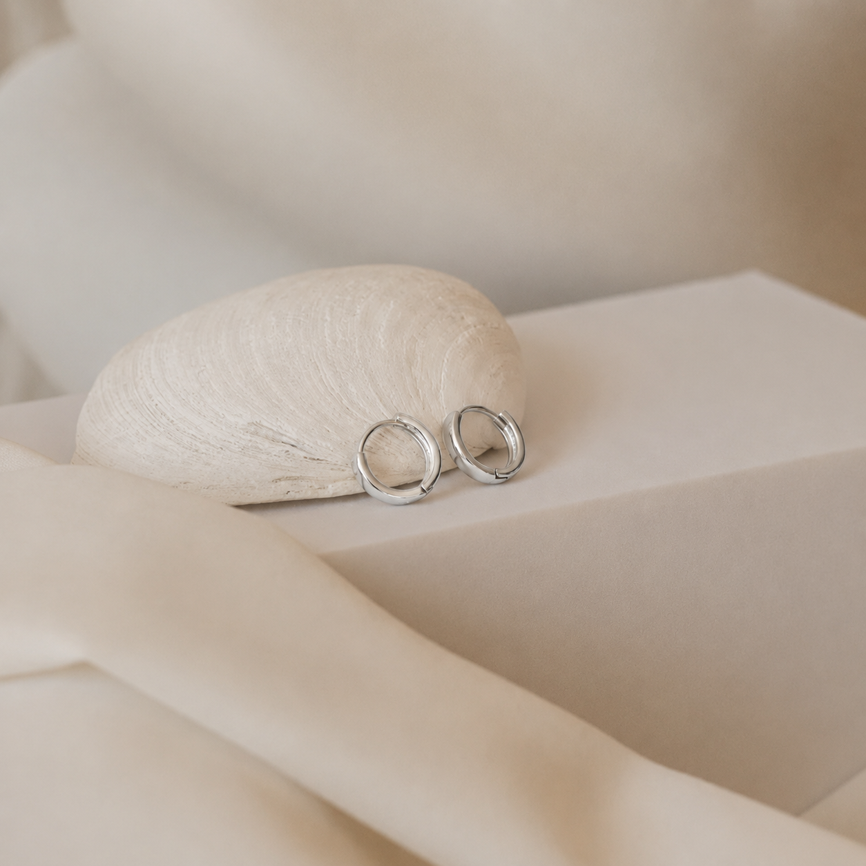 Silver earrings on a soft beige fabric background