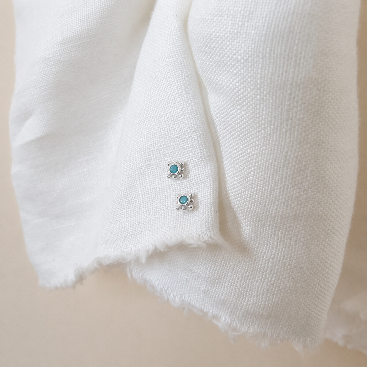 Pair of turquoise gemstone earrings on a white fabric background