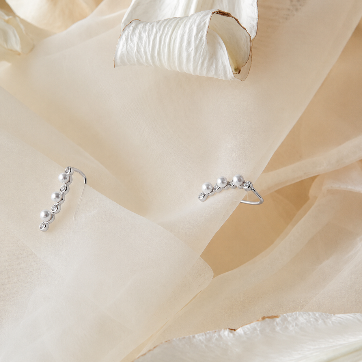Silver earrings with pearls on a soft beige fabric background