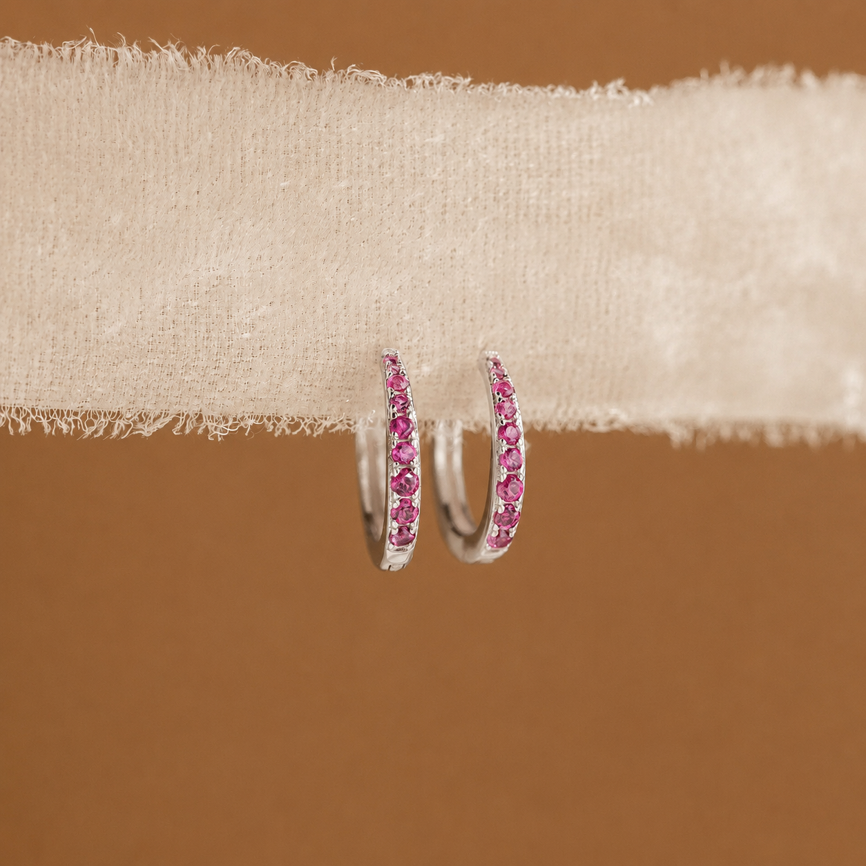 Pink hoop earrings on a beige fabric background