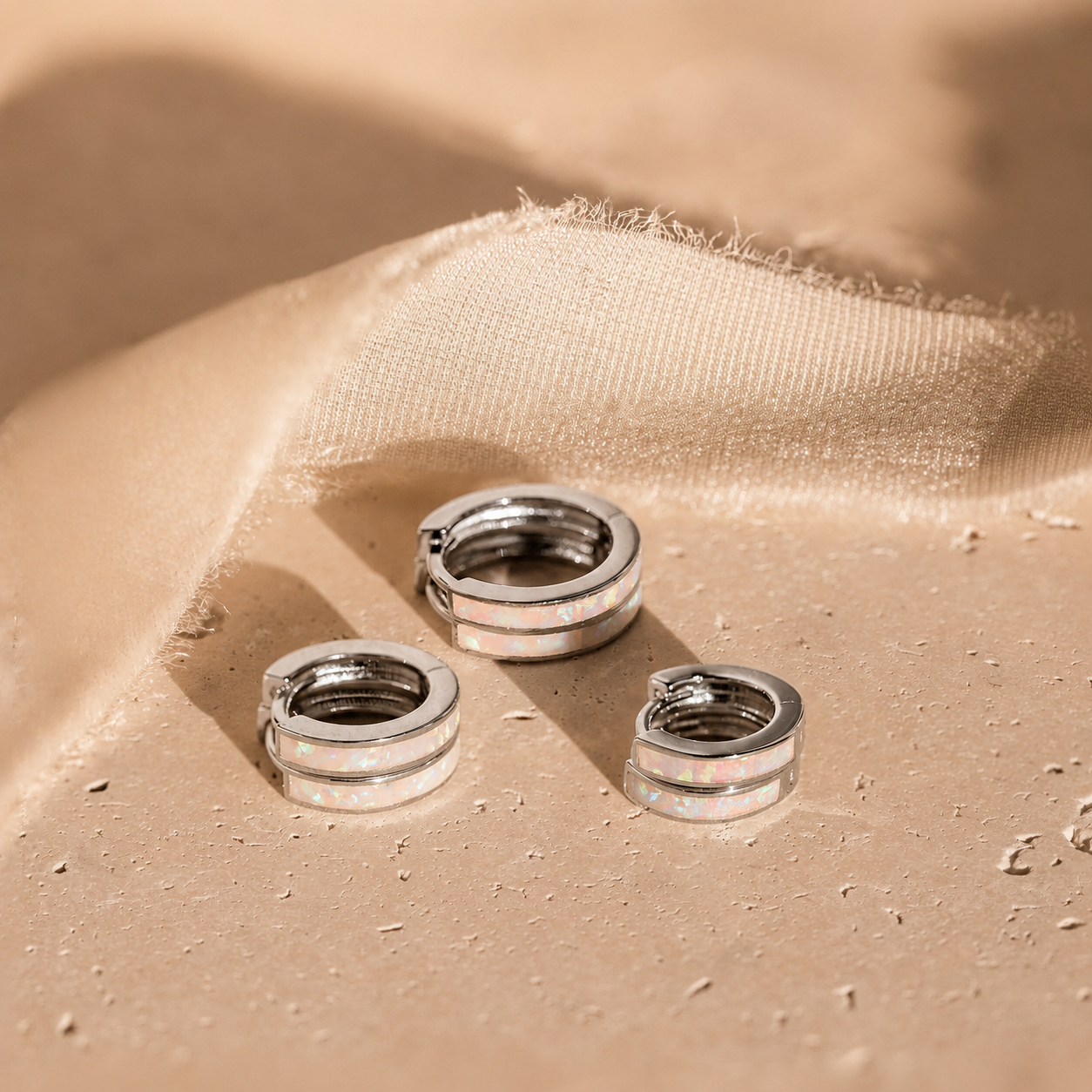 Three silver hoop earrings on a beige fabric surface