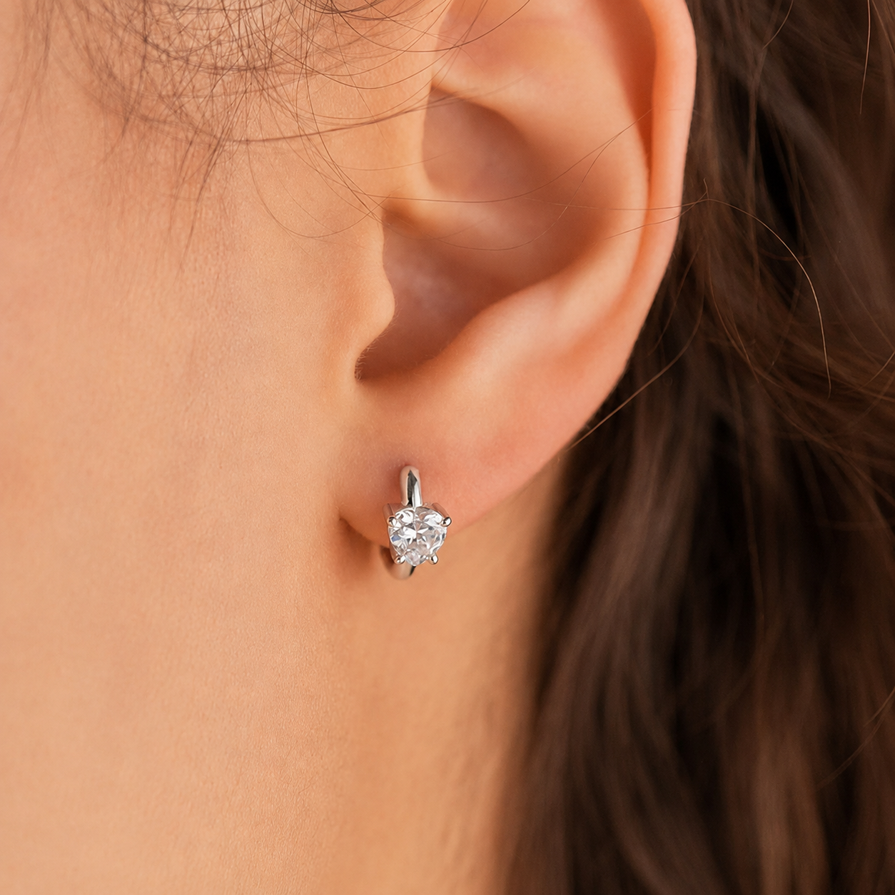Close-up of an ear wearing a diamond earring with hair partially obscuring the view.