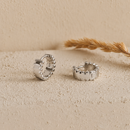 Silver hoop earrings on a textured beige surface with a natural background