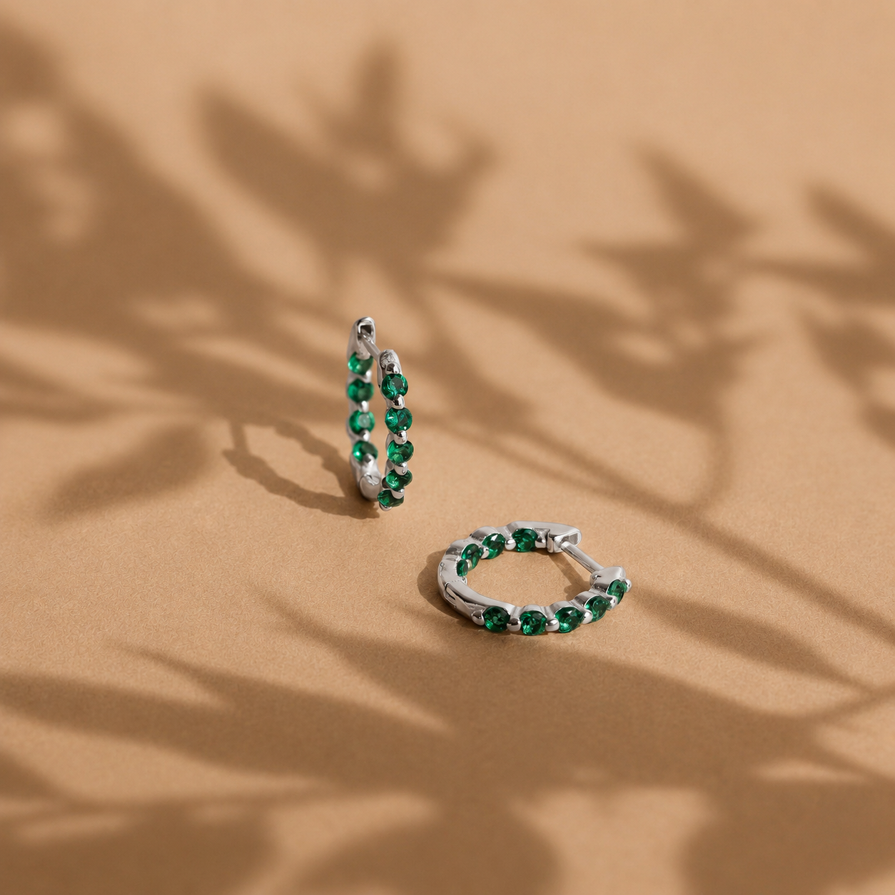 Pair of silver hoop earrings with green gemstones on a beige background
