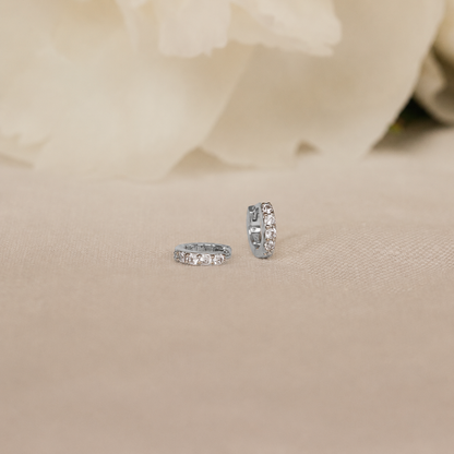 Pair of silver hoop earrings with small diamonds on a beige fabric background