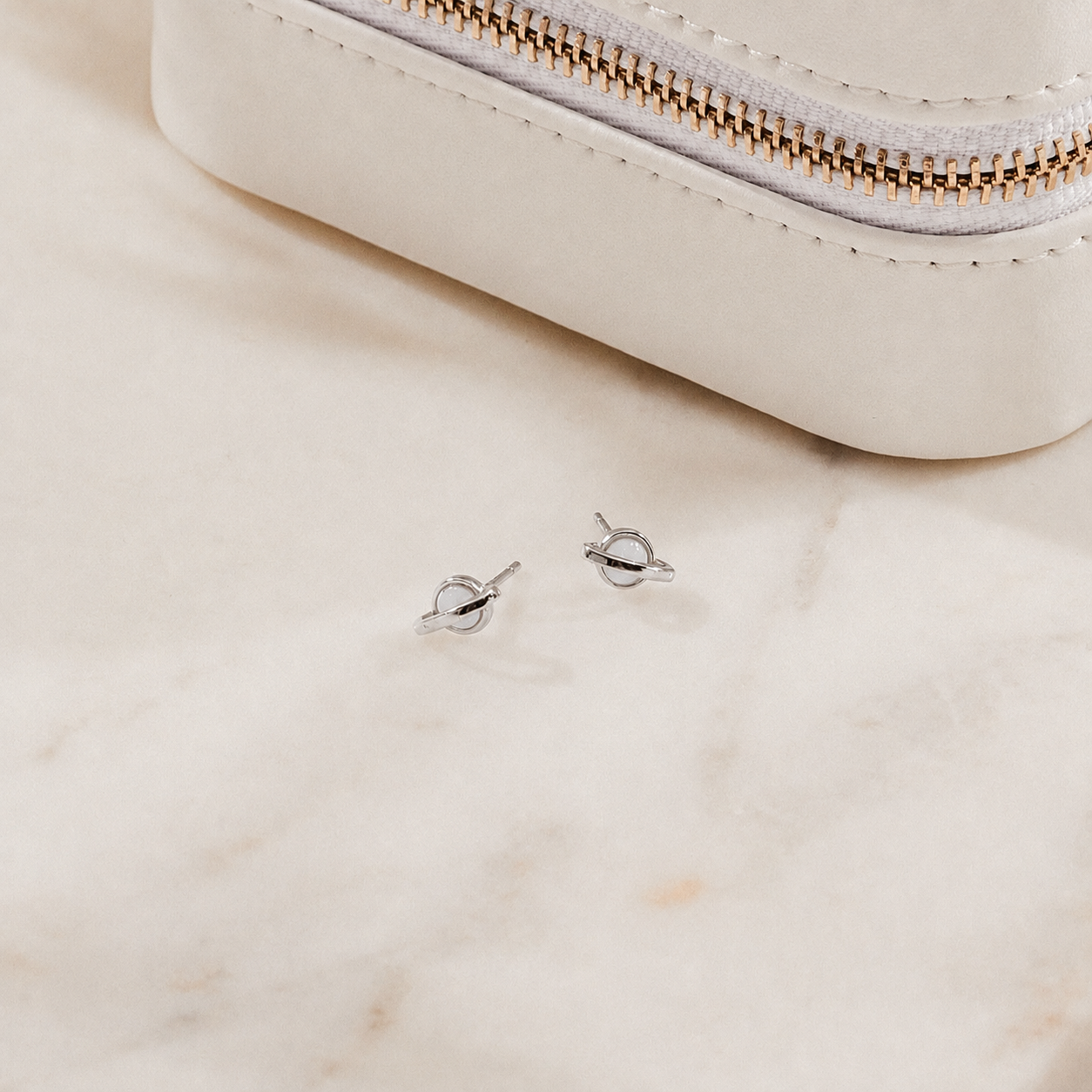 Silver earrings on a marble surface with a white pouch in the background