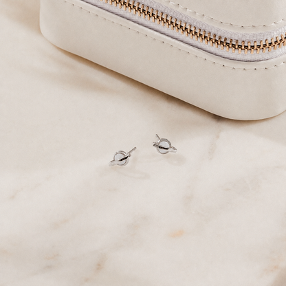 Silver earrings on a marble surface with a white pouch in the background