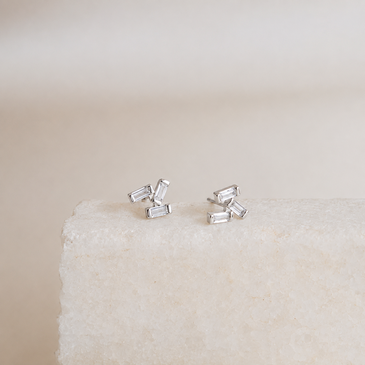 Silver baguette cut stud earrings on a textured beige surface