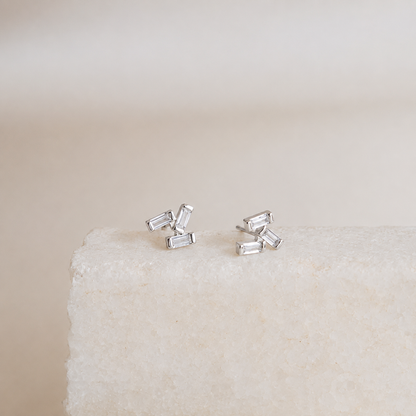 Silver baguette cut stud earrings on a textured beige surface