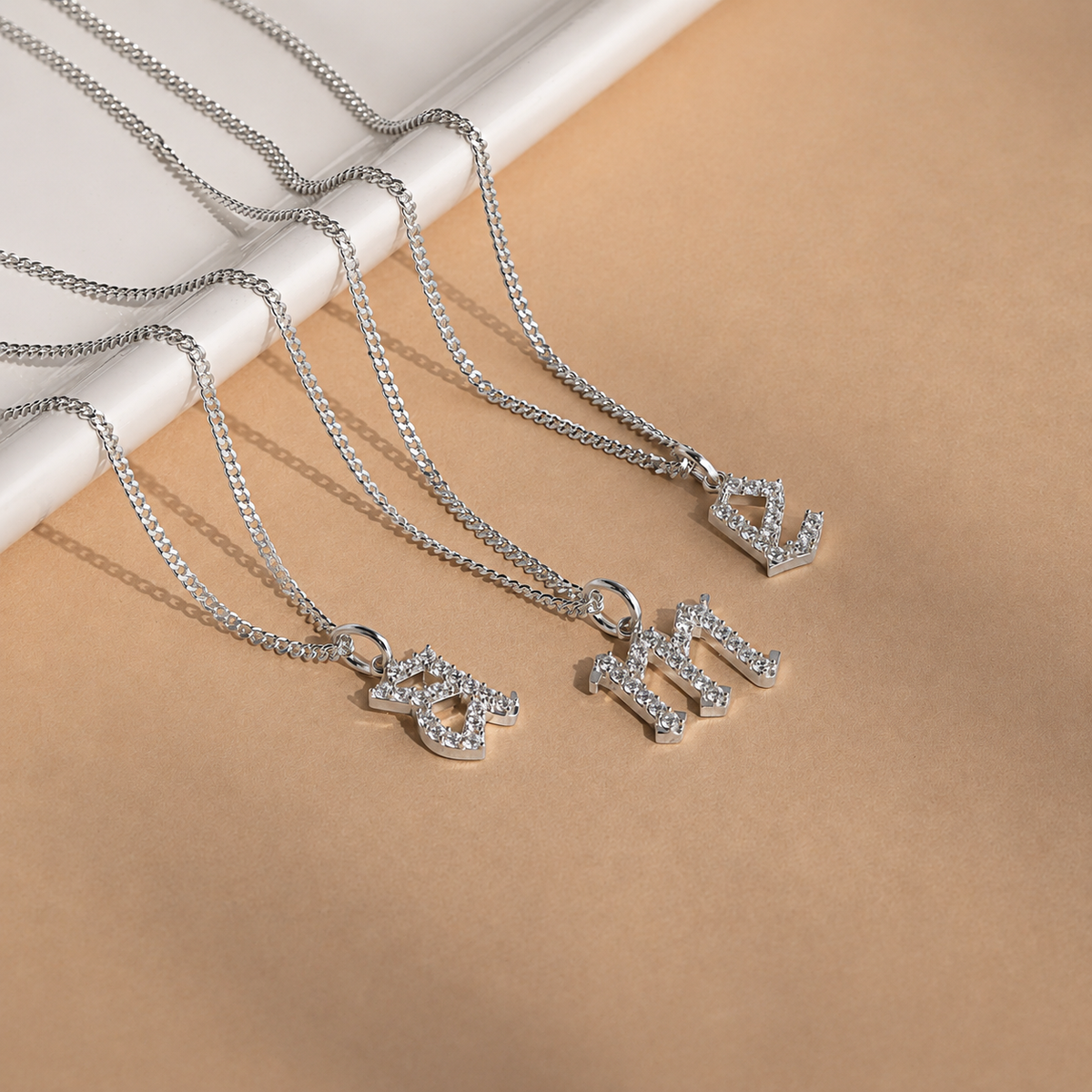 Silver necklaces with letter pendants on a beige surface