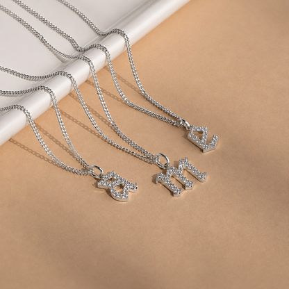 Silver necklaces with letter pendants on a beige surface