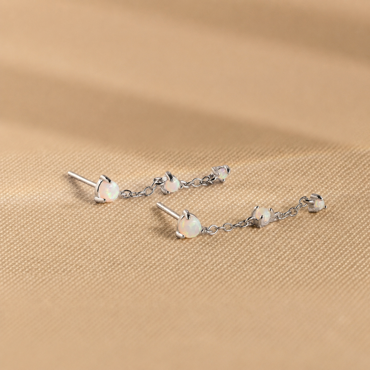 Silver earrings with opal stones on a beige fabric background