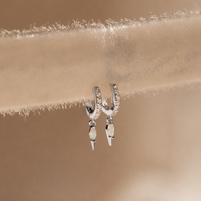 Silver hoop earrings with dangling elements on a beige fabric background