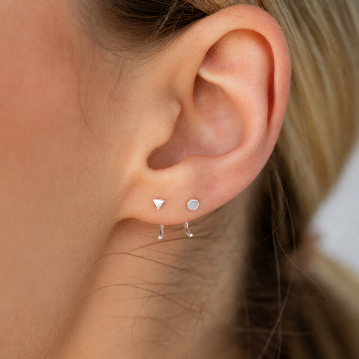 Close-up of an ear wearing three small silver earrings.