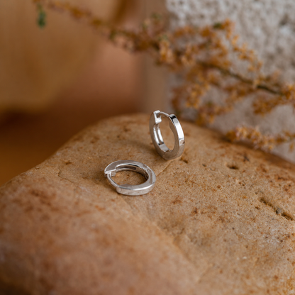 Silver hoop earrings on a textured stone surface with a blurred natural background