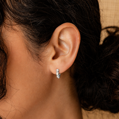 Close-up of an ear wearing a silver earring with dark hair and blurred background