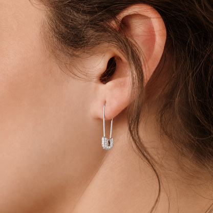 Close-up of an ear wearing a silver hoop earring with a small heart charm.