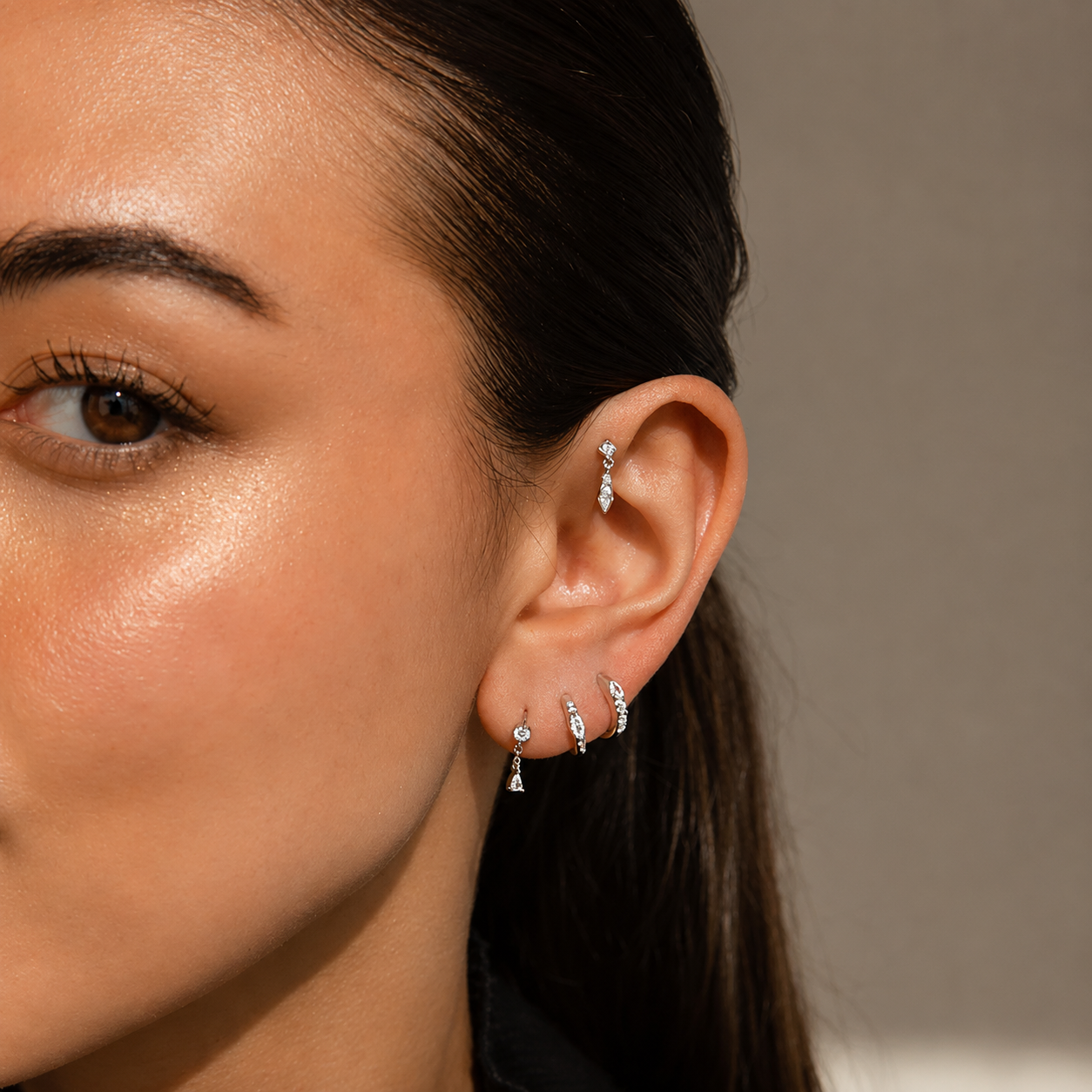 Close-up of a woman's ear with multiple earrings against a neutral background