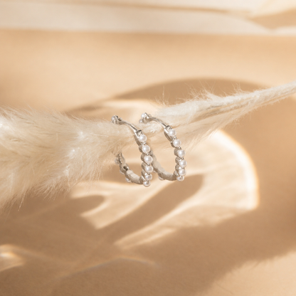 Silver hoop earrings with pearls on a beige surface