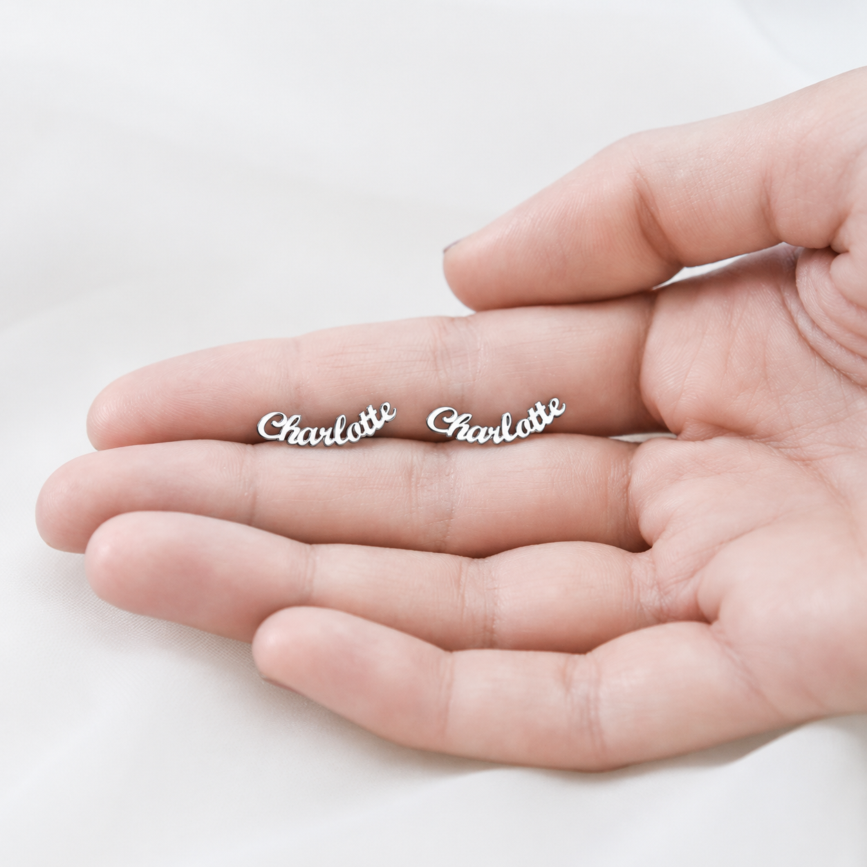 Silver 'Charlotte' earrings held in a hand on a light background
