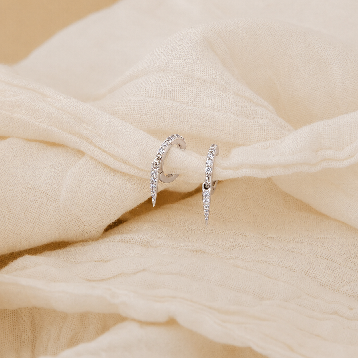 Silver hoop earrings on a beige fabric background