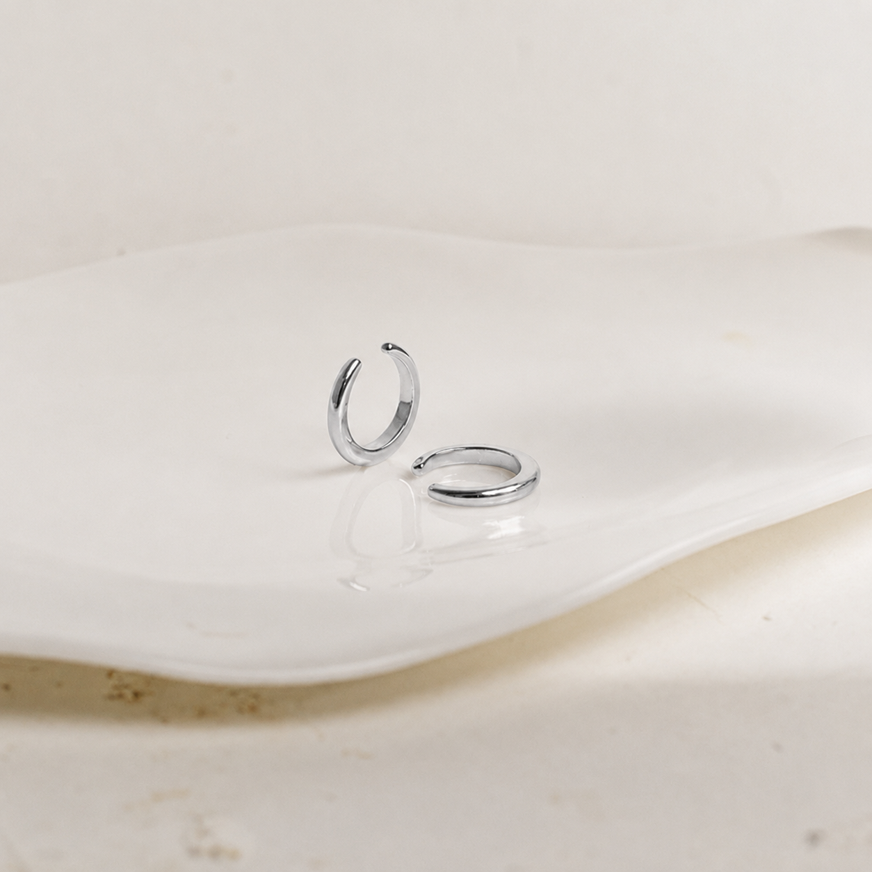 Two silver hoop earrings on a white ceramic plate