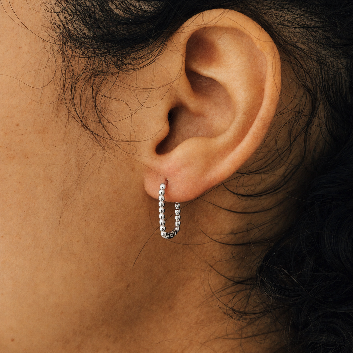 Close-up of an ear wearing a silver hoop earring with dark hair partially visible.