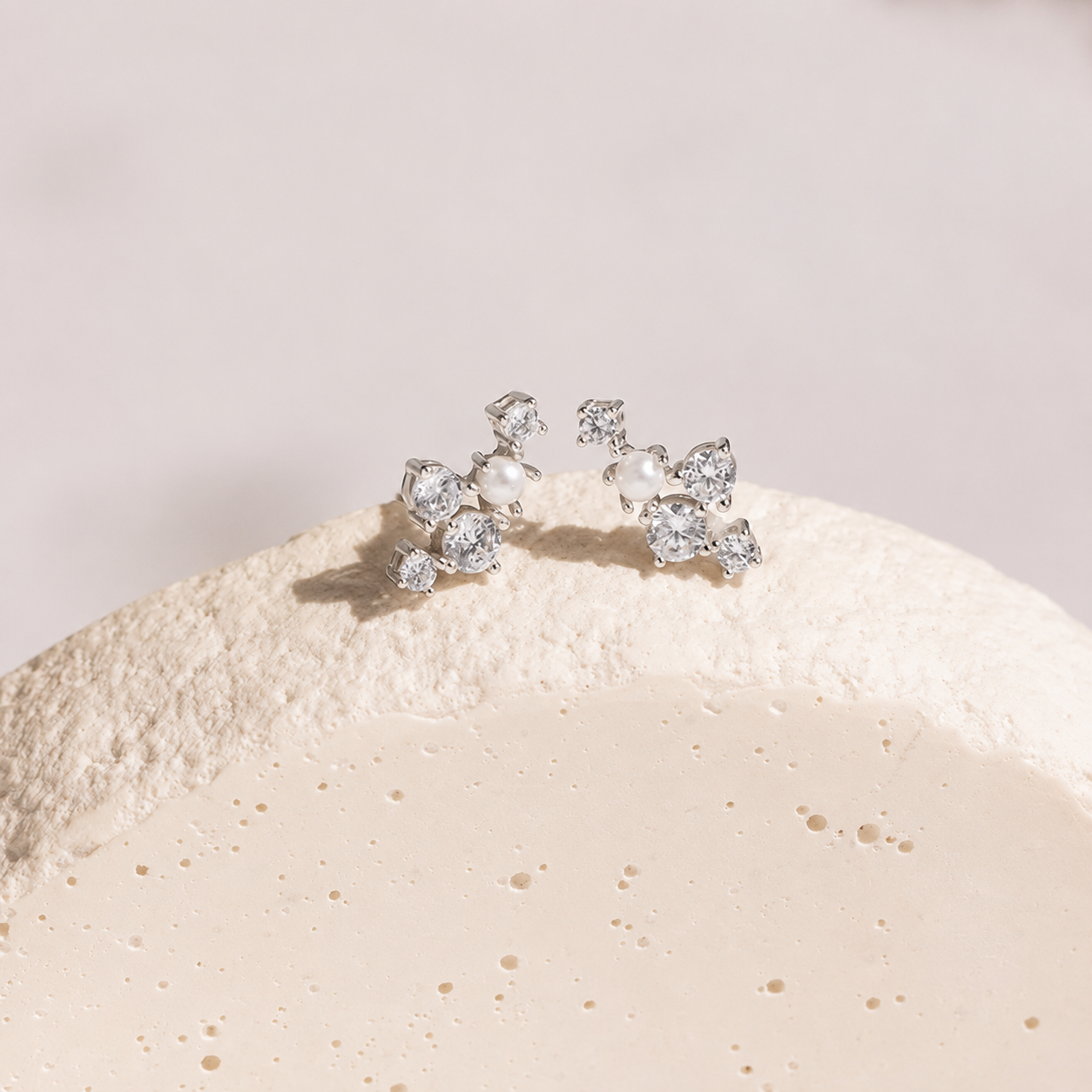 Silver earrings with clear stones on a textured beige surface