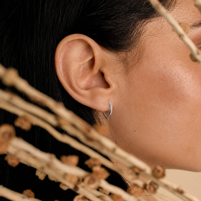 Close-up of an ear wearing a silver hoop earring with a blurred natural background