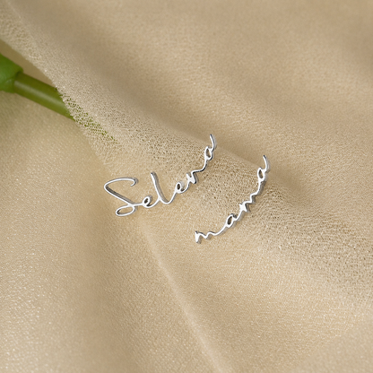 Silver earrings with 'Selena' and 'Mom' engraved on a beige fabric background